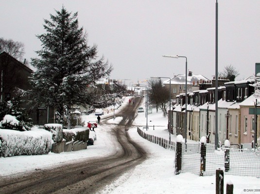 View from the far end of Neilston Main Street
The row of terraced houses on the left were built at the turn of the last century to house workers in Crofthead Mill.  Some of the names of the surrounding streets are related to the Boer War campaign of the time.   In the distance, above the centre of the road, the Church Tower can just be seen.  [url=http://www.streetmap.co.uk/map.srf?X=247375&Y=656852&A=Y&Z=110/] Map location. [/url]
