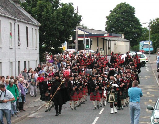 Pipe Bands Parading in High Street at the East Meets West event during Neilston Live!
The Neilston & District Pipe Band flanks each side of the Tokyo Pipe Band with the Royal Pipe Band of the deputation of Ourense bring up the rear.   Robbs Garage is in the background.
