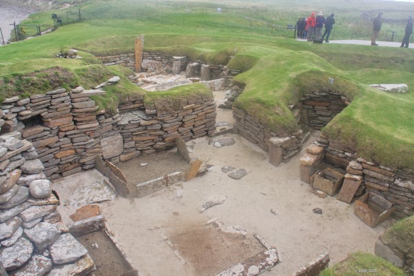 Skara Brae Neolithic Settlement, House 5
House 5 is one of the larger later houses at Skara Brae with a number of internal features. The floor area of around 40 sq meters is organised into rectangular beds around a central hearth. Opposite the entrance which leads off the main east-west passageway is a intramural compartment and lined floor-tanks.
