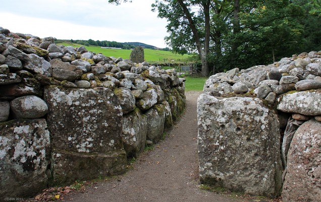Looking out from the South West Passage Grave at Clava
As with the other cairns at Clava the entrance passage is aligned south west to catch the mid winter sun rise.  The grave would have have been covered over with large flag stones with a very low entrance passage that you would have to crawl through.  On the right hand side you can see carved 'cup' marks, the meaning of these is unknown.  You can see one of the 11 stones that ring the cairn to the left of the entrance in the distance.
