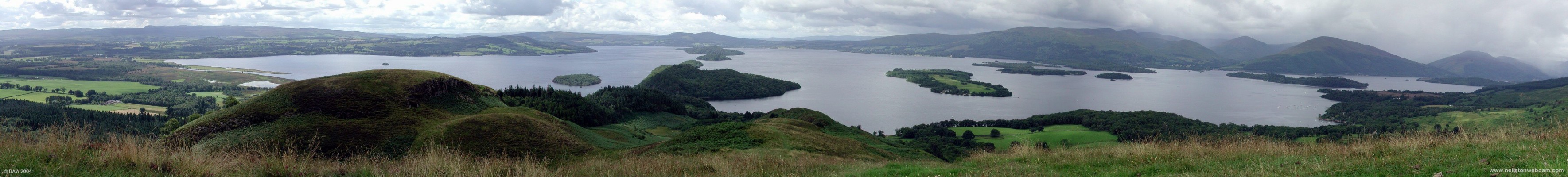 Panoramic view from Conic Hill, Loch Lomond
A view over the southern end of Loch Lomond.  The photo is taken standing on the divide between Lowland and Highlind Scotland, the Highland Fault.  If you look closely you'll see a dip in the ground in the foreground around the middle of the picture that lines up with 3 or 4  of the Islands and also a dip in the Hills in the Distance.  A typical summer day with showers heading in from the North.  
