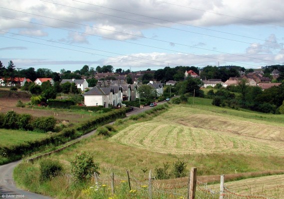 Springfield Road
This is a view from the edge of the village looking back along Springfield Road.  The white houses in the centre of the picture were built for Mill workers.  The red tiled roofs behind these houses is a new housing development that is built on the fields where the Neilston Show was held until about 1999.
