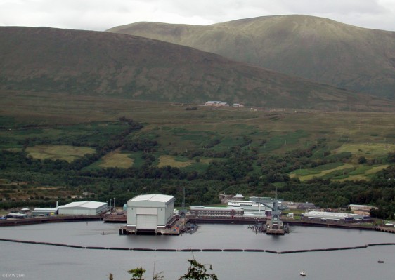 The Trident Submarine Jetties and Ship-lift at Faslane Base, Gareloch
On the right hand side of the ship lift building there are 3 jetties specifically for the Vanguard class Trident Submarines of the Royal Navy.  Two can be seen berthed here.  One is always on patrol, one is in maintenance/refit and the remaining two are on stand-by.  The ship-lift is capable of lifting a 16,000 ton Vanguard submarine in "operational" condition completely out of the water for maintenance.  The floating boom around the area is an attempt to stop protestors gaining access to the secure area.

